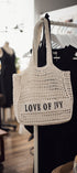 Crocheted bag with 'LOVE OF IVY' text hanging on a rack in a store setting.