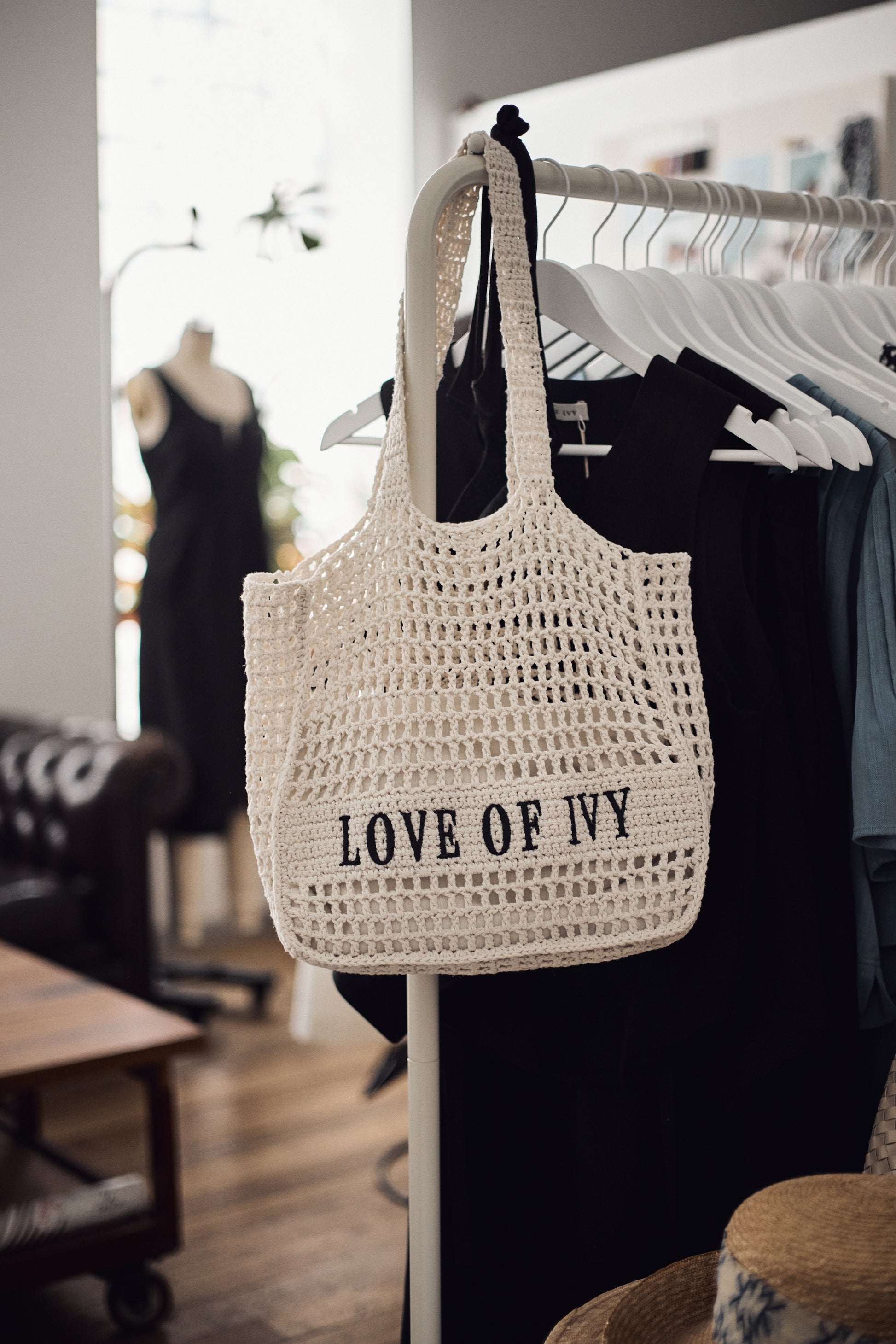 Crocheted bag with 'LOVE OF IVY' text hanging on a rack in a store setting.