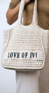 White woven bag with 'LOVE OF IVY' text held by a person wearing a beige top and white pants.