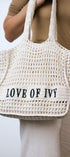 White woven bag with 'LOVE OF IVY' text held by a person wearing a beige top and white pants.