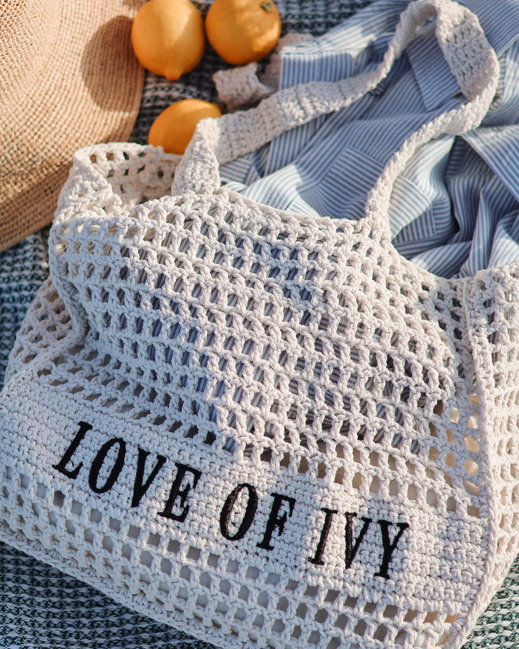 Mesh bag with 'LOVE OF IVY' text on a textured surface with oranges and a hat.
