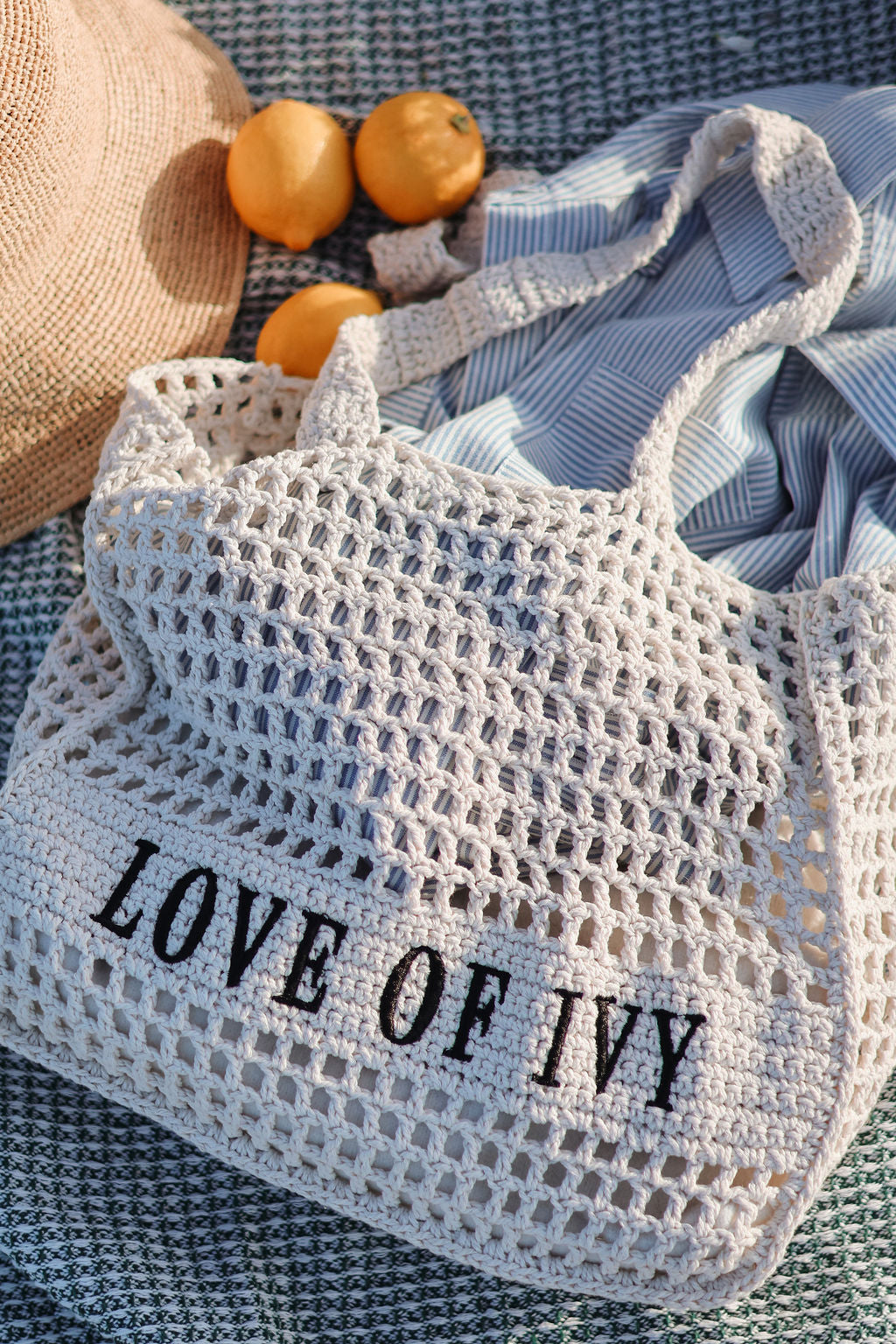 Mesh bag with 'LOVE OF IVY' text on a textured surface with oranges and a hat.