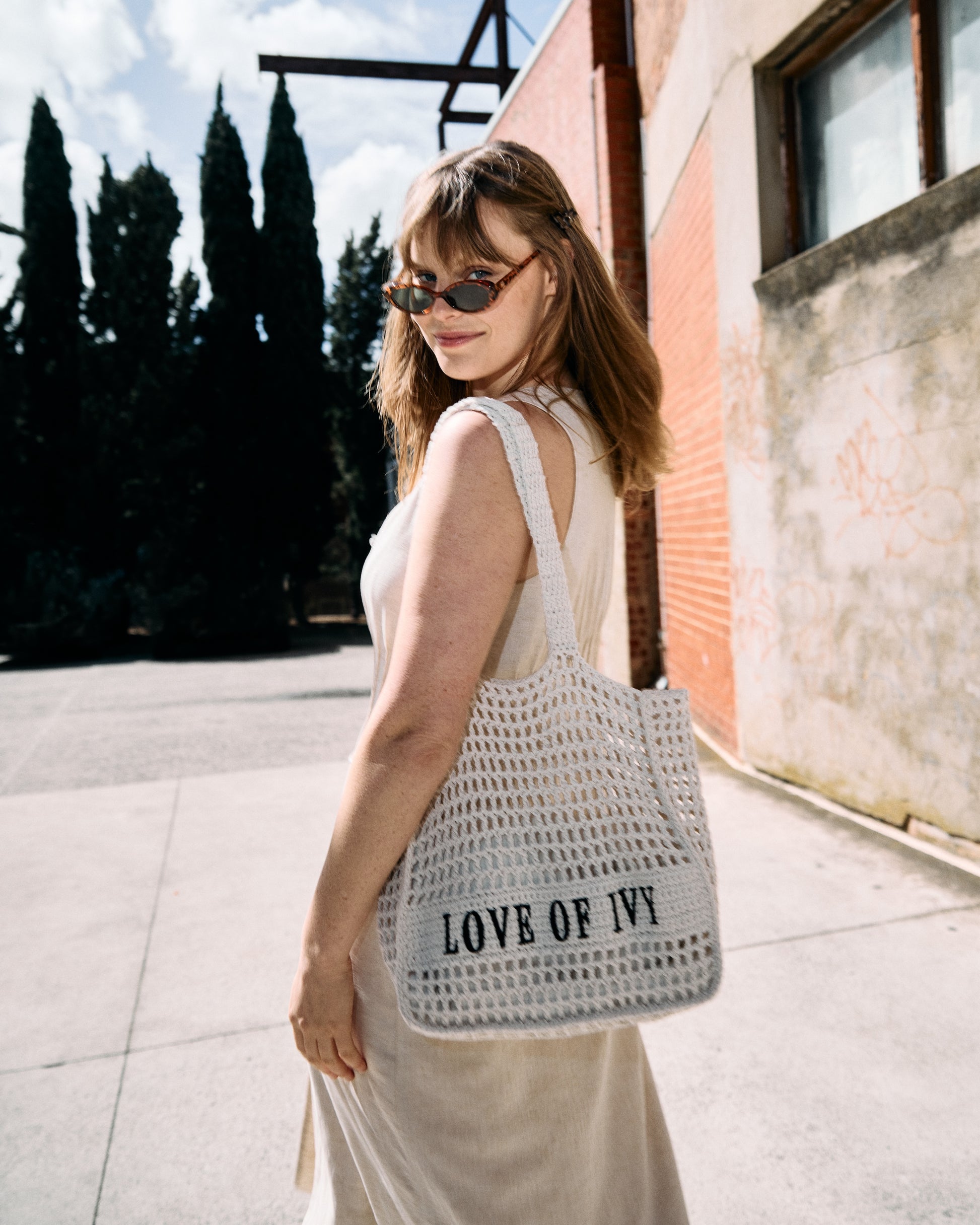Woman holding a woven handbag with 'LOVE OF IVY' branding outdoors.
