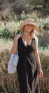 Woman in a black dress and straw hat standing in a natural setting