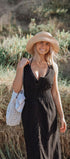 Woman in a black dress and straw hat standing in a natural setting