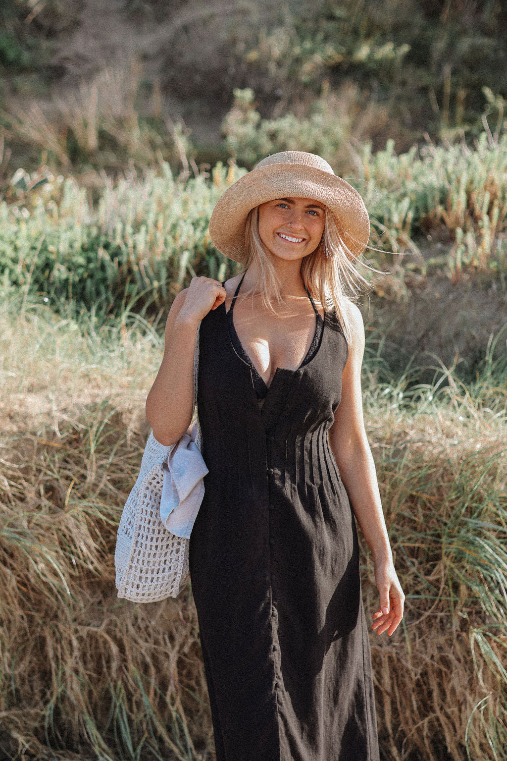 Woman in a black dress and straw hat standing in a natural setting