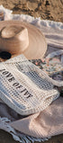 Woven bag with 'LOVE OF IVY' text on a beach setting with a hat, sunglasses, and orange.