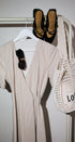 Beige dress, black shoes, and a white mesh bag on a rack against a white wall.