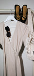 Beige dress, black shoes, and a white mesh bag on a rack against a white wall.