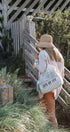 Woman with a straw hat and a tote bag with 'LOVE OF FLY' text standing near a wooden fence.
