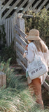 Woman with a straw hat and a tote bag with 'LOVE OF FLY' text standing near a wooden fence.