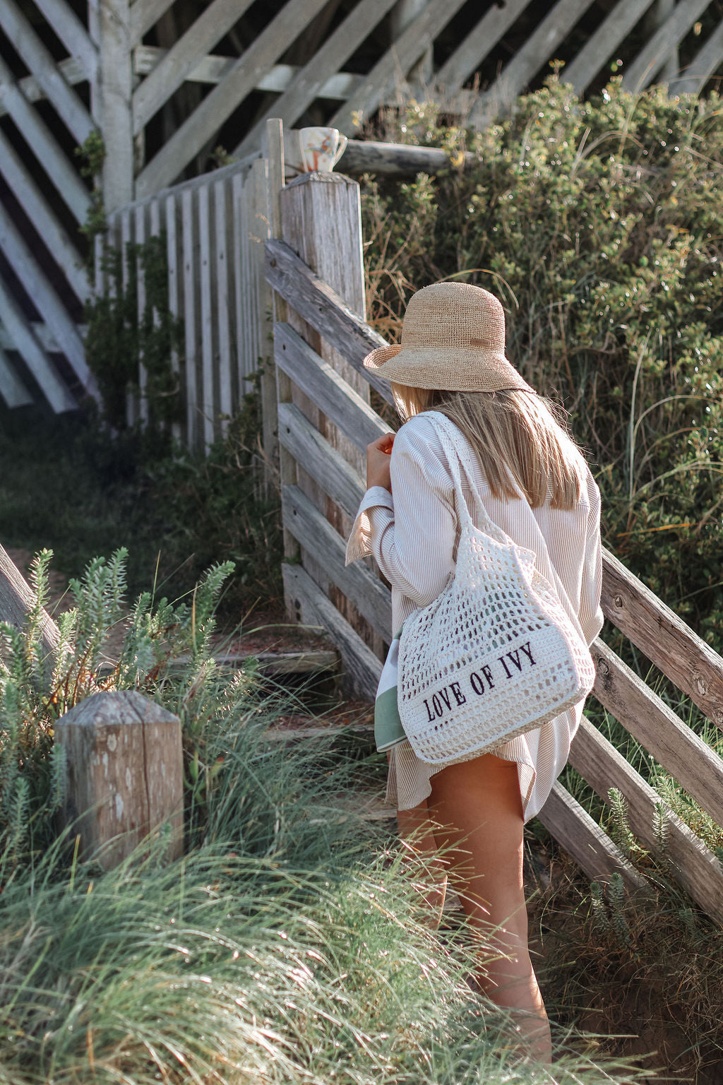 Woman with a straw hat and a tote bag with 'LOVE OF FLY' text standing near a wooden fence.
