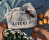 White crochet bag with 'LOVE OF IVY' text on a blue textured surface with oranges and a hat.