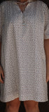A person wearing a loose short-sleeve tunic dress with a small dark floral print on a light cream background, featuring a tie-neck detail.