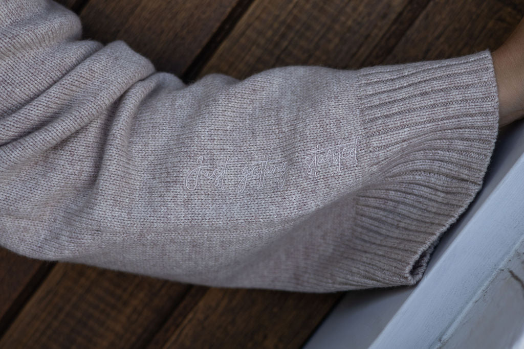 Close-up of a person wearing a beige sweater with embroidery