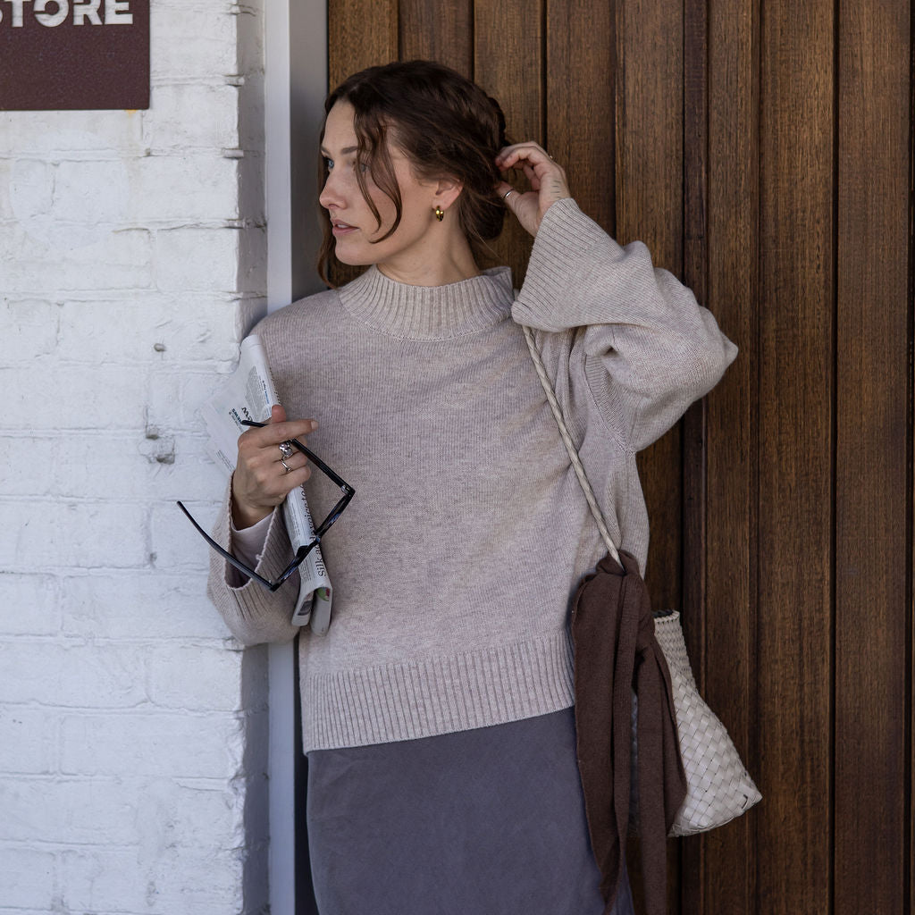 Woman adjusting her hair against a wooden wall with a store sign.
