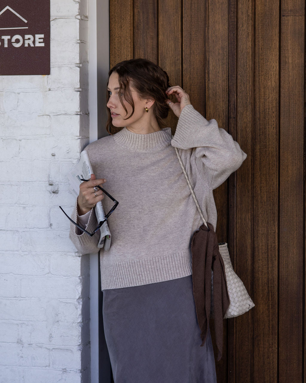 Woman adjusting her hair against a wooden wall with a store sign.