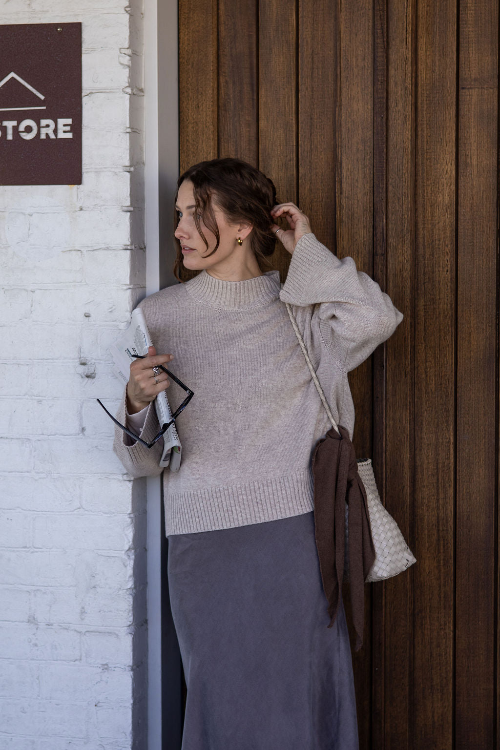 Woman adjusting her hair against a wooden wall with a store sign.