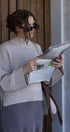 Woman reading a newspaper outdoors, wearing sunglasses and a light sweater.