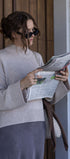 Woman reading a newspaper outdoors, wearing sunglasses and a light sweater.