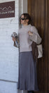 Woman standing outside a store named 'Gold Grain Store' holding a magazine.