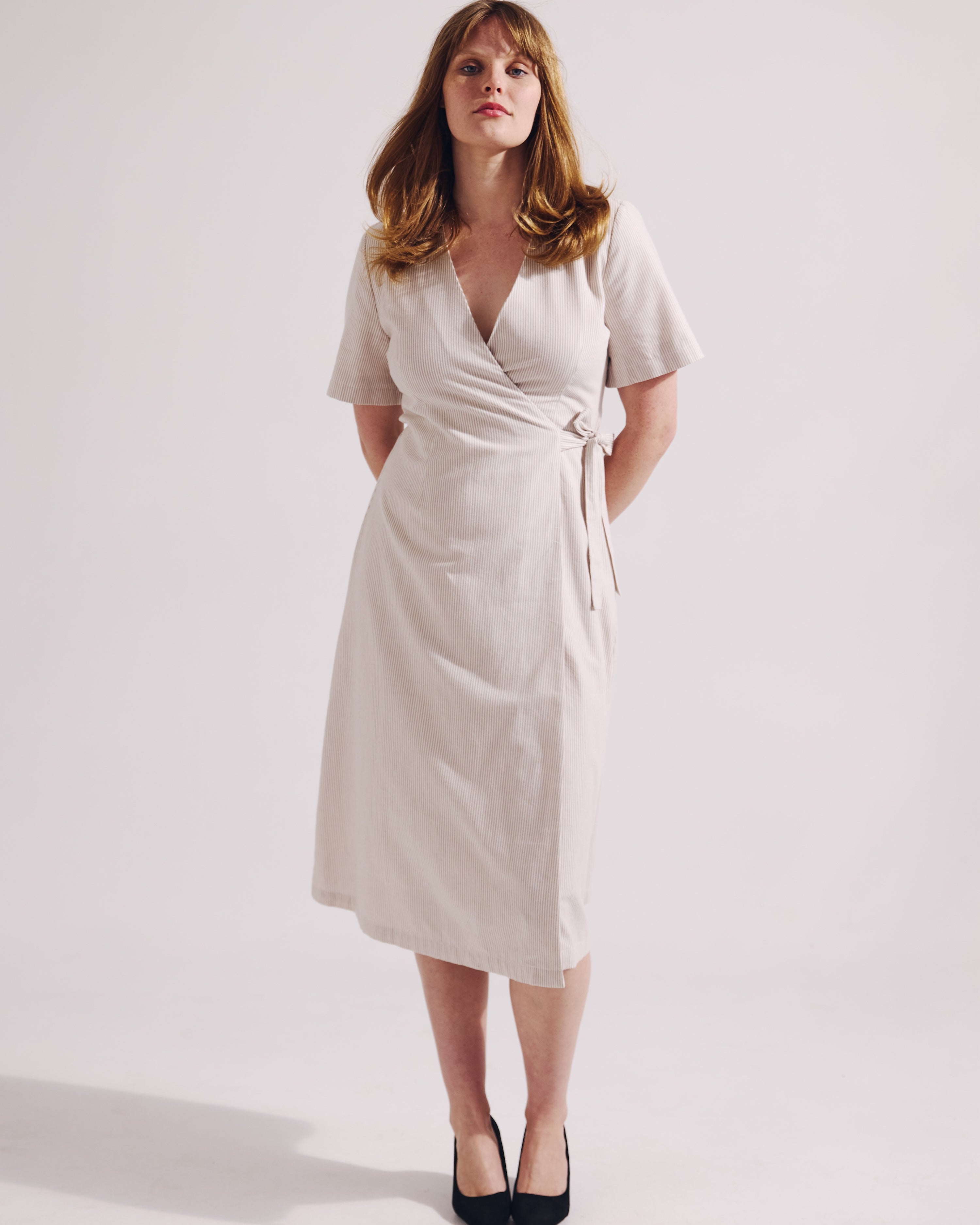 Woman wearing a white wrap dress on a plain background