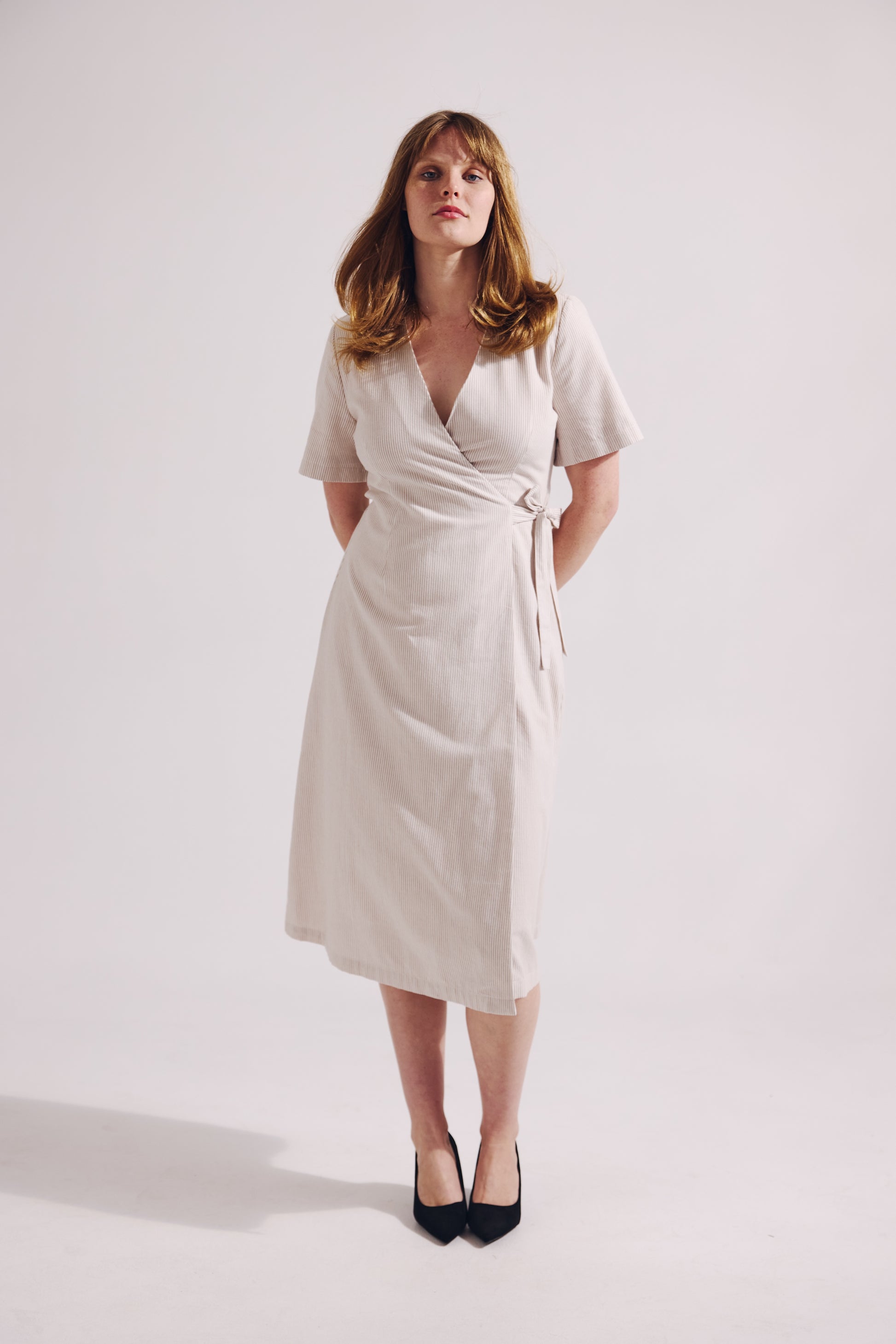 Woman wearing a white wrap dress on a plain background