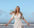 Woman in a white dress standing on a beach with a clear blue sky.