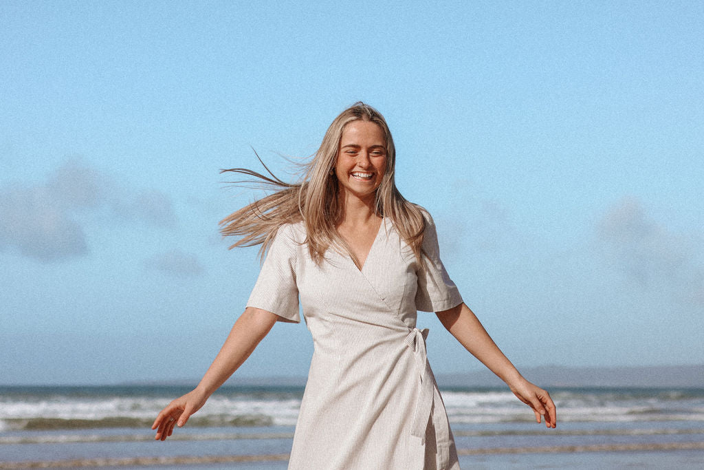 Woman in a white dress standing on a beach with a clear blue sky.