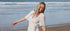 Woman in a white dress standing on a beach with ocean waves in the background