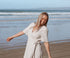 Woman in a white dress standing on a beach with ocean waves in the background