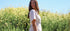 Woman in a white dress standing in a field of yellow flowers with a clear blue sky.