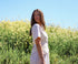 Woman in a white dress standing in a field of yellow flowers with a clear blue sky.