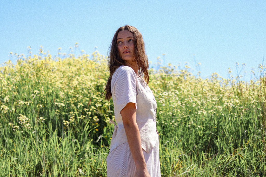 Woman in a white dress standing in a field of yellow flowers with a clear blue sky.
