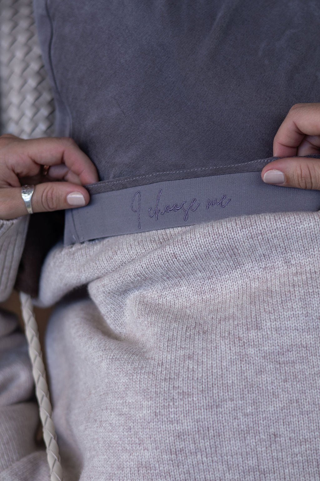 Close-up of a person adjusting a gray sweatshirt with embroidery.