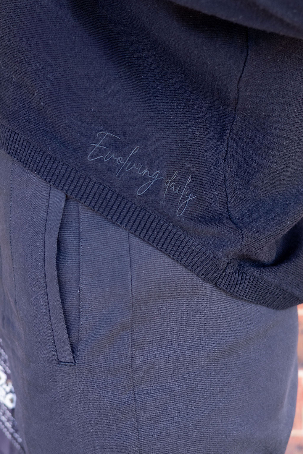 black knit top with 'Evolving Daily' embroidery on a blurred background