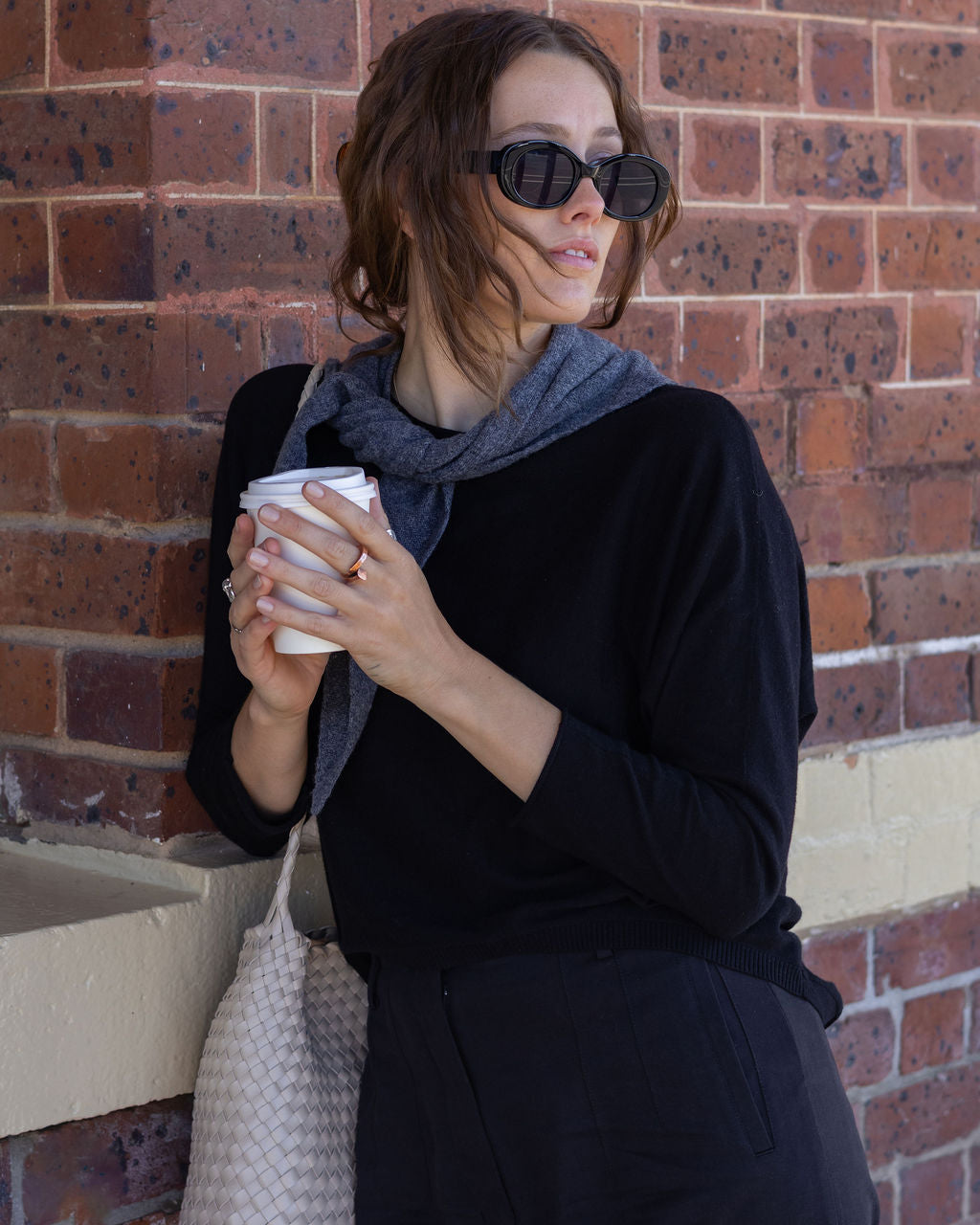 Woman holding a coffee cup against a brick wall