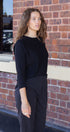 Woman wearing a black outfit standing against a brick wall.