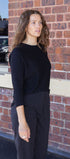 Woman wearing a black outfit standing against a brick wall.