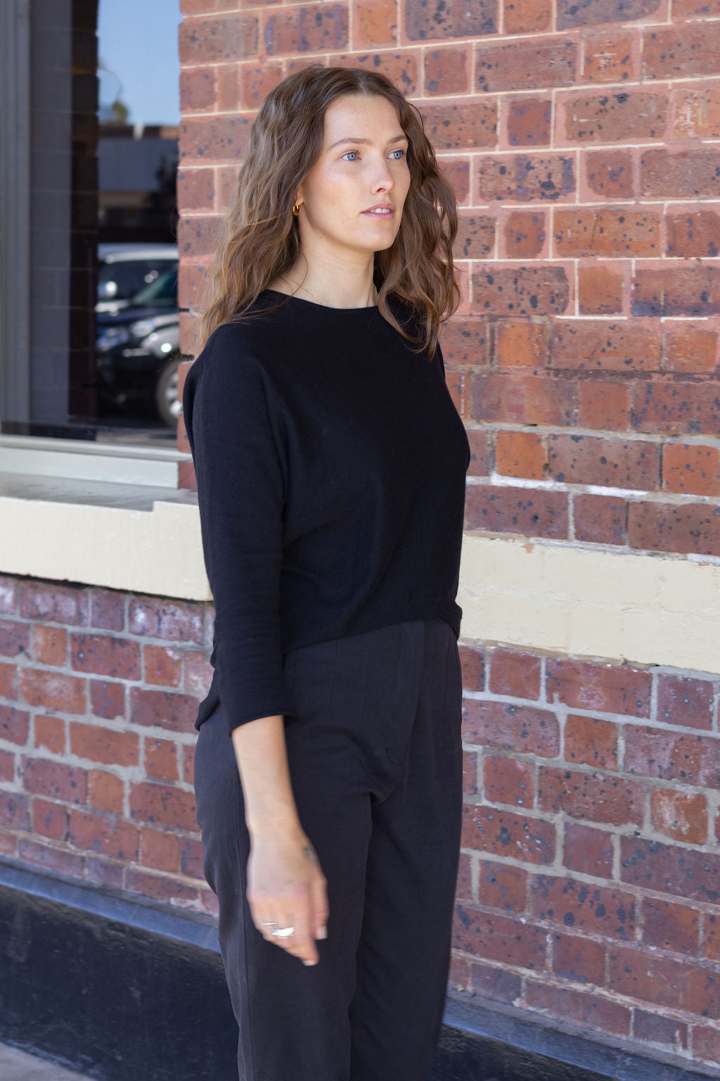 Woman wearing a black outfit standing against a brick wall.