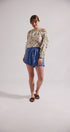 Woman wearing a patterned top and blue shorts on a plain background