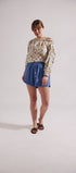 Woman wearing a patterned top and blue shorts on a plain background