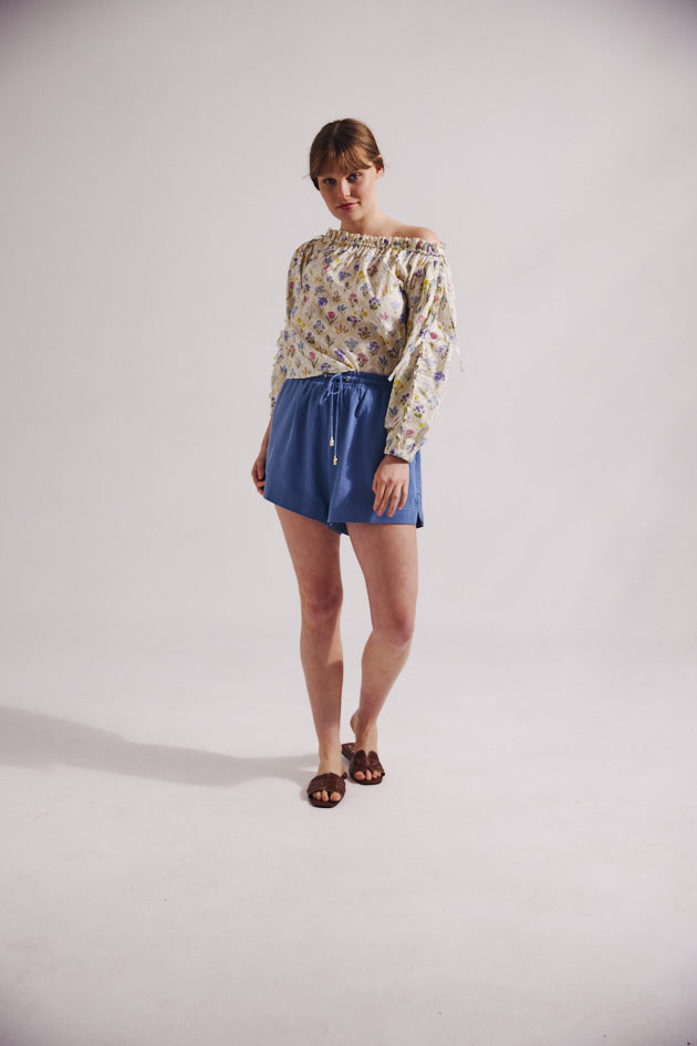 Woman wearing a patterned top and blue shorts on a plain background