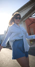 Woman in white shirt and blue shorts standing outdoors on a sunny day.