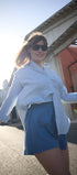 Woman in white shirt and blue shorts standing outdoors on a sunny day.