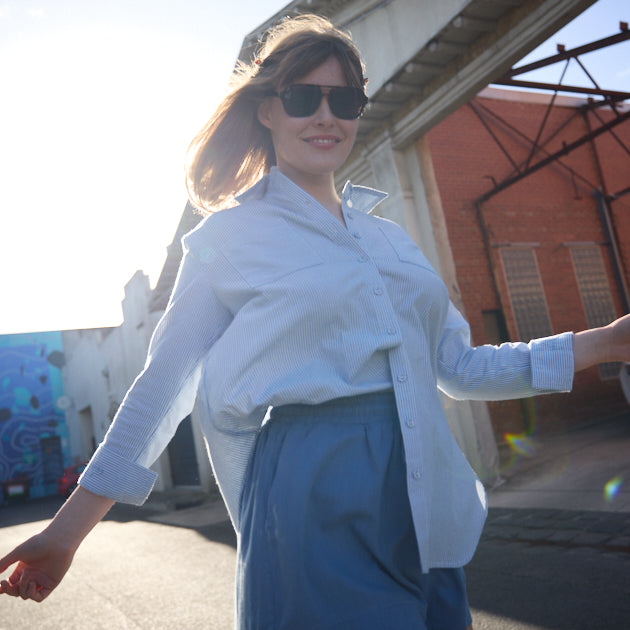 Woman in white shirt and blue shorts standing outdoors on a sunny day.
