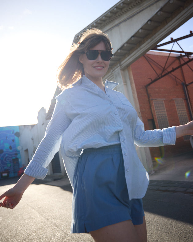Woman in white shirt and blue shorts standing outdoors on a sunny day.
