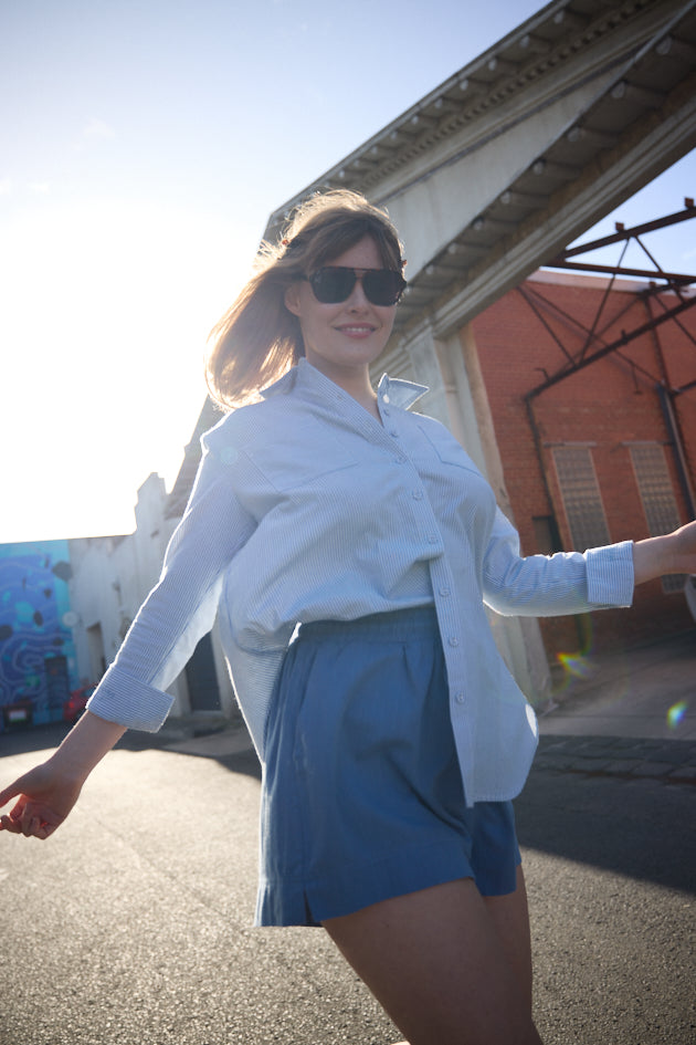 Woman in white shirt and blue shorts standing outdoors on a sunny day.
