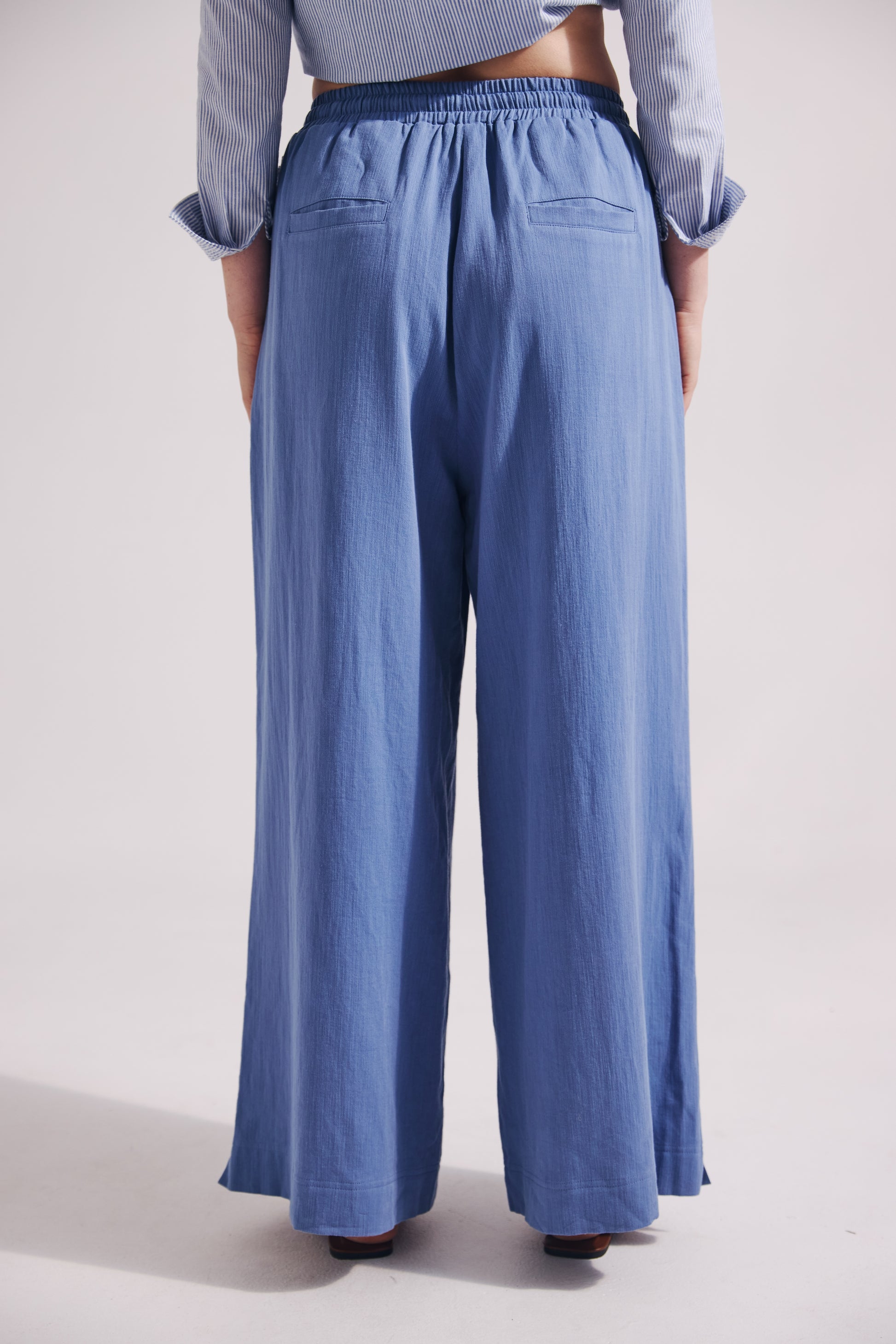 Person wearing blue wide-leg pants and a light blue shirt on a white background