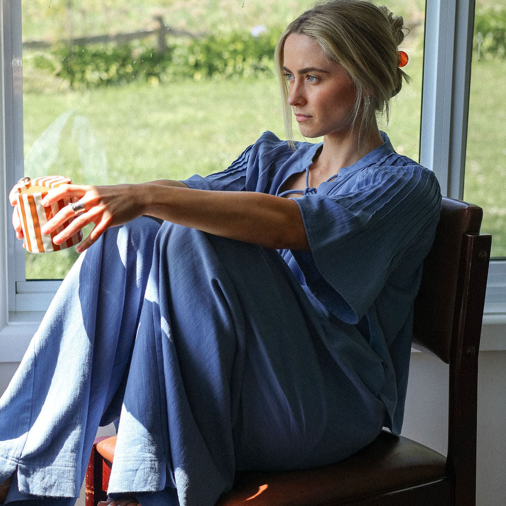 Woman sitting on a chair by a window holding a bowl, with a scenic view outside.